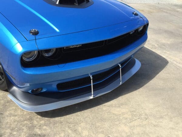 Front view of a blue Dodge Challenger parked in a lot, featuring a custom front splitter and hood pins.