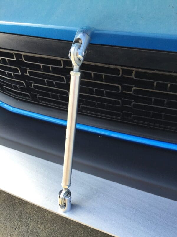 The front bumper of a blue car features a metal handle attached vertically, with a detailed view of the grille.