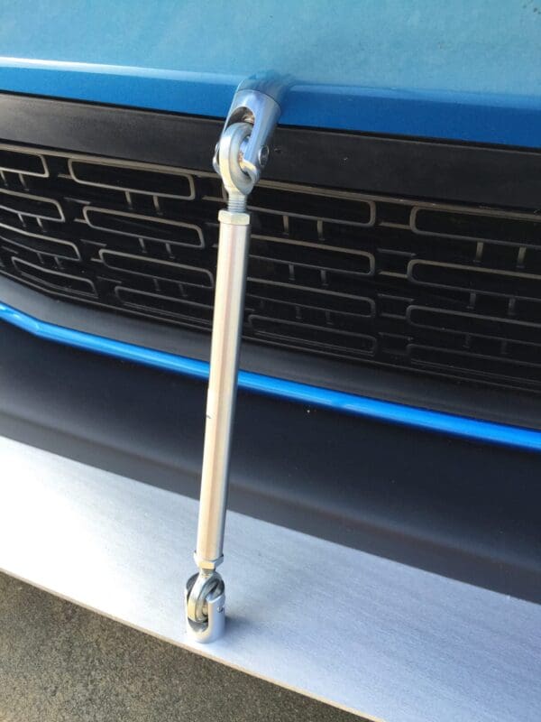 The front bumper of a blue sports car with a silver support rod connecting the bumper to the body.