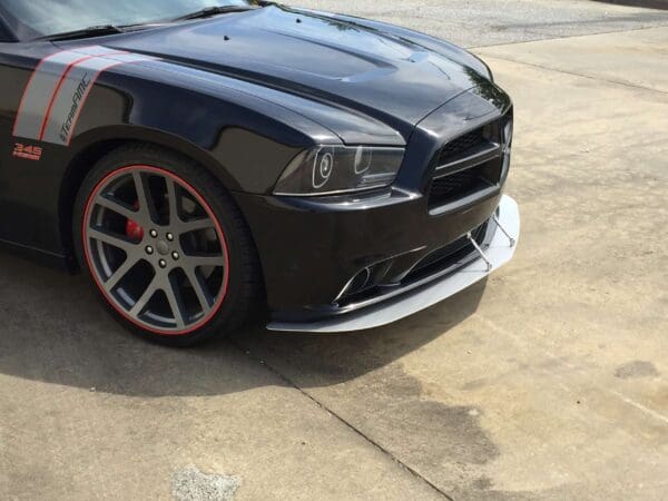 A black sports car with custom decals and red-trimmed wheels is parked in a parking lot.