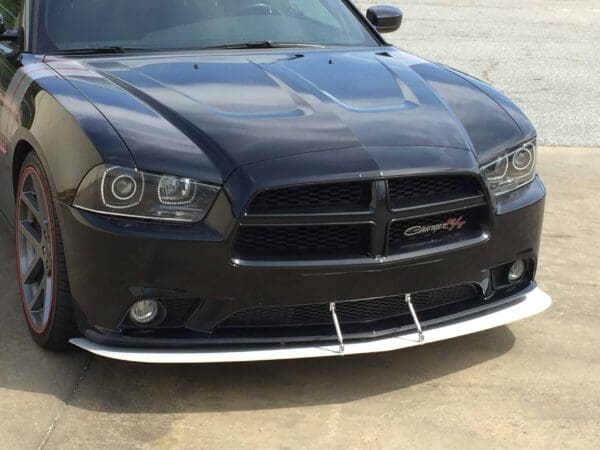 A black Dodge Charger parked in a parking lot, featuring sporty red-accented wheels and a front splitter.