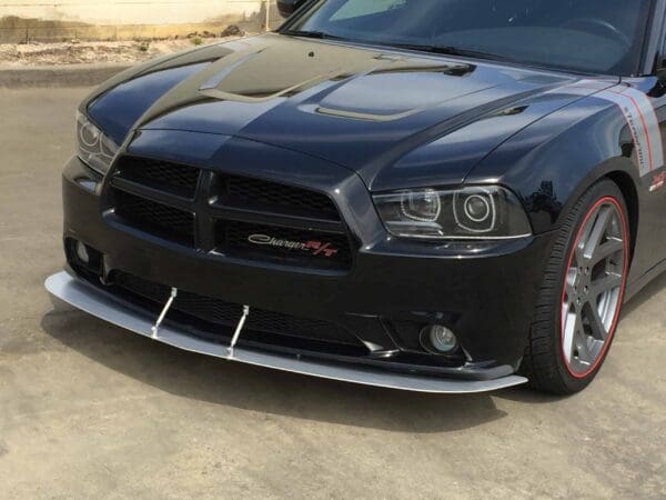 A black Dodge Charger R/T with red-accented rims parked in a lot, showcasing its front grille and sleek design.