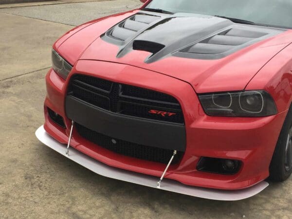 A red Dodge Charger SRT with a black hood and front splitter parked in a lot.