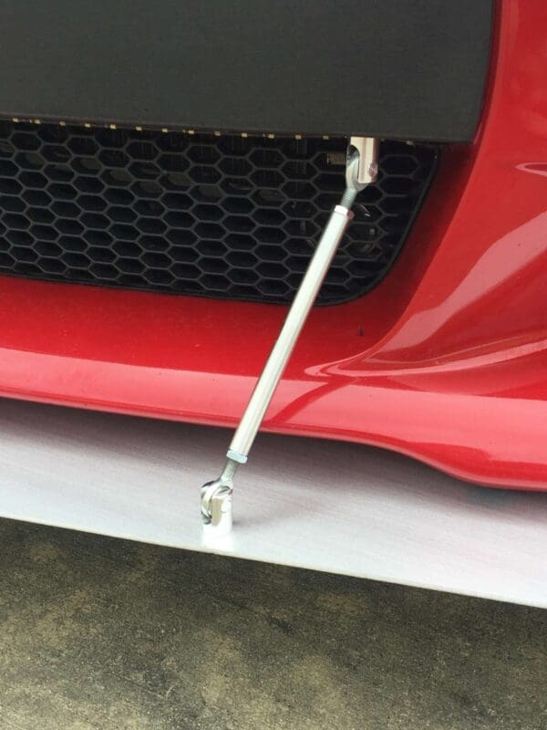 Close-up of the front bumper of a red sports car, featuring a honeycomb grille and metal support rod.