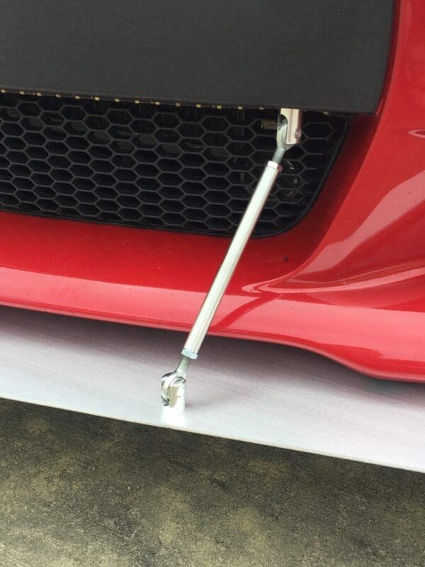 Front bumper close-up of a red sports car with a silver support rod and black grille detailing.