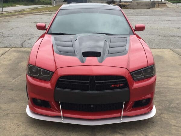 A red Dodge Charger SRT with a black hood and front splitter parked in a lot.