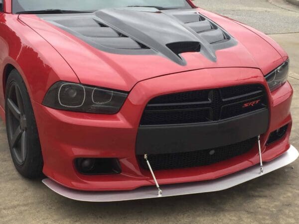 A red sports car with a black hood and SRT badge, featuring sleek headlights and a front splitter, is parked on a concrete surface.