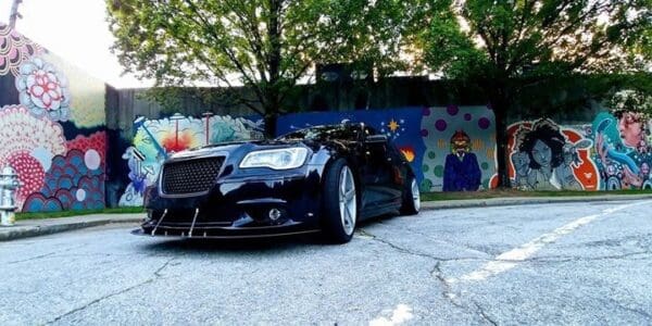 A black car parked in front of a graffiti covered wall