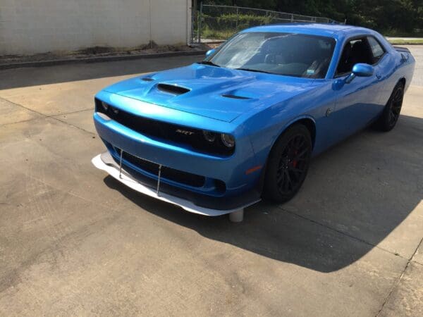 A blue sports car, Dodge Challenger SRT, parked on a driveway in sunlight.