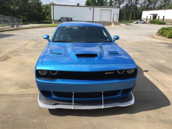 A blue SRT car parked in a lot, with industrial buildings and trees in the background.