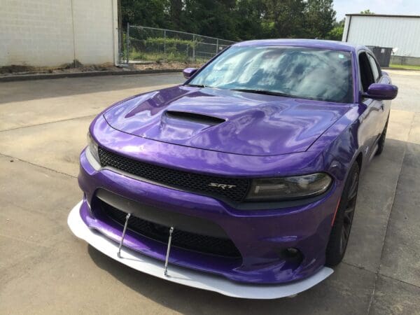 A purple car parked in front of a building with a fence and trees in the background.
