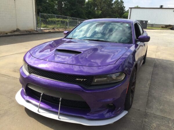 A purple sports car, featuring a hood scoop, parked in front of a building.