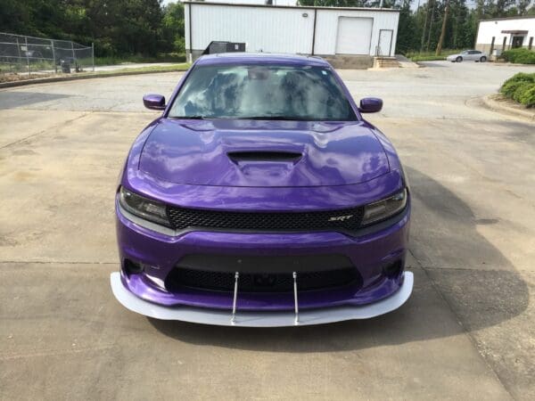 A purple Dodge Charger SRT parked in a parking lot, with a warehouse in the background.