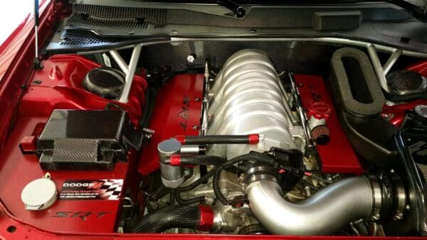 Engine compartment of a red Dodge Charger SRT8, featuring a 6.1L Hemi engine with red accents and carbon fiber components.
