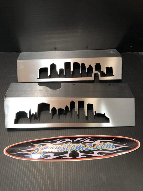 Metal signs with city skyline designs on a table, above a "3zcustomz.com" logo sticker.