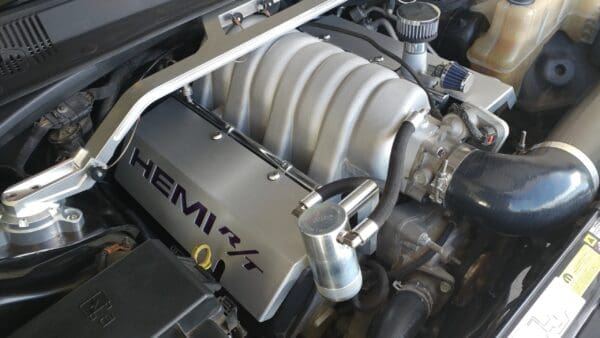 Close-up of a car engine featuring "HEMI R/T" branding on the cover, showcasing its components and design.