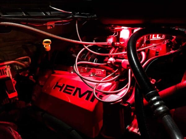 Car engine illuminated by red light, featuring "HEMI" branding and visible cables and components.