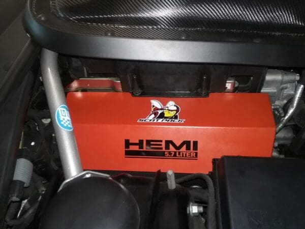 Close-up of a car engine featuring a HEMI 5.7 liter label and Scat Pack logo on an orange component.
