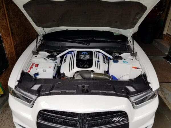 Open car hood revealing a white engine bay with labeled V8 parts, featuring a 5.7L engine.