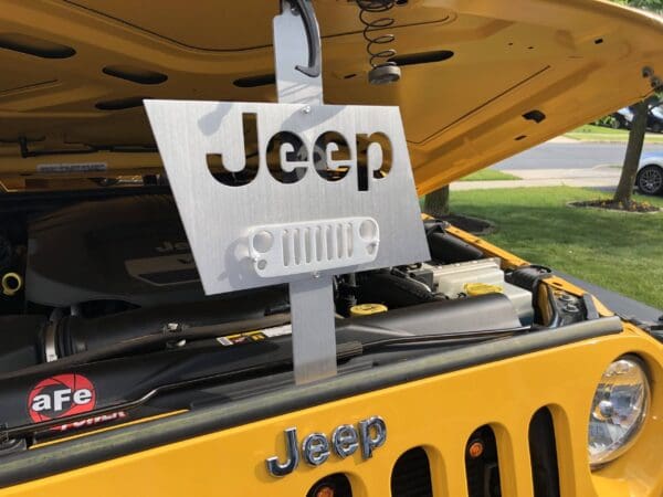 Custom Jeep grille sign hanging on an open yellow Jeep hood showing engine.