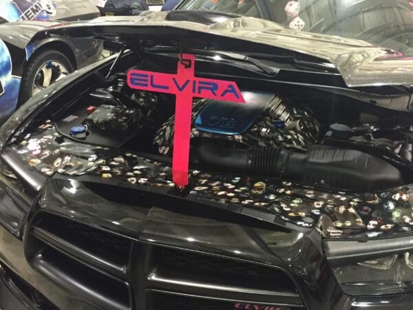 Black car with open hood, engine visible, and 'ELVIRA' on red crossbar.