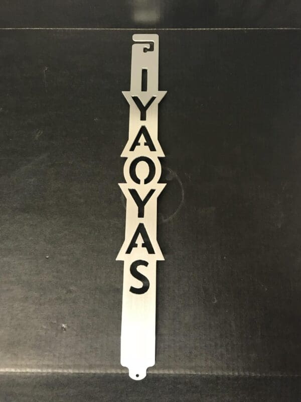 Vertical metal ornament with letters "IYAOYAS" on a dark background.