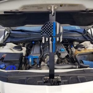 A white car with its hood open, displaying an American flag design with a blue line on a metal piece in front of the engine.