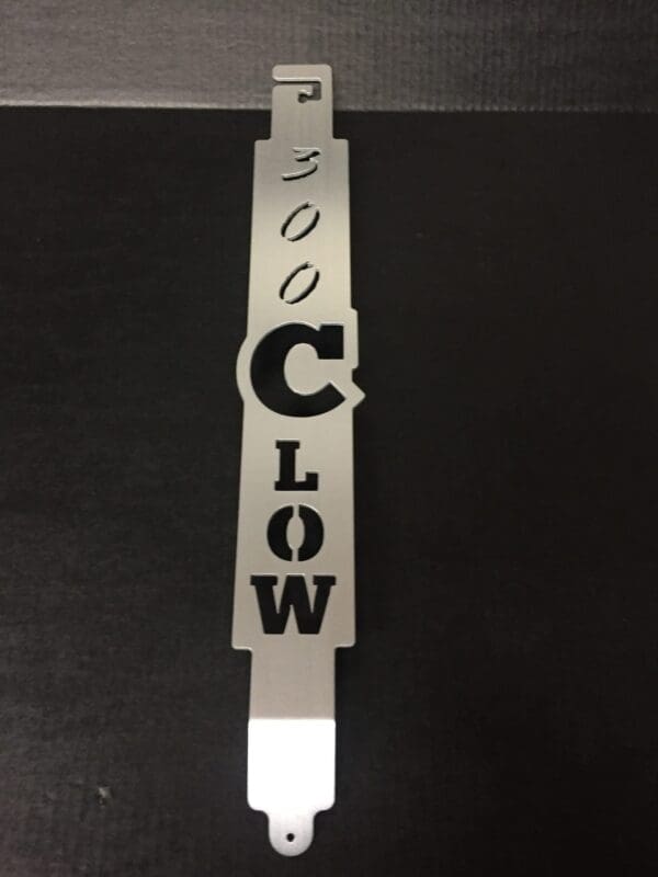 etal tool with cutout letters spelling "300 C LOW" on a dark surface.