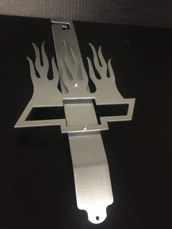 Silver flame-shaped hood prop with the chevrolet emblem on it.