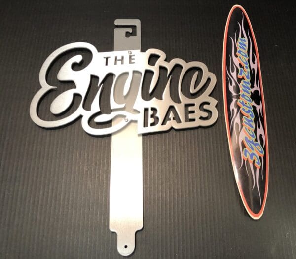 Custom metal Hood Prop and sticker signage with stylized text on a dark surface.