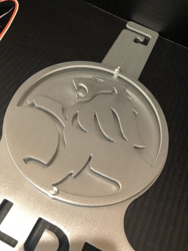 Silver emblem with a stylized bat design on a black surface.