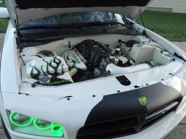 A white sports car with its hood open, revealing a customized engine with "HEMI" and flame designs.