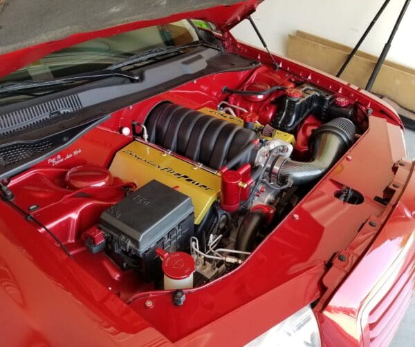 The engine compartment of a red sports car, featuring a Chrysler Firepower engine with custom detailing and performance parts.