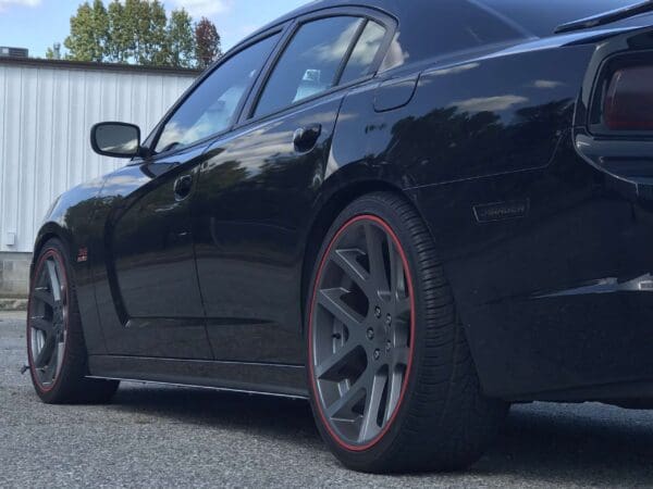 A black Dodge Charger parked in a lot, featuring red-striped wheels and a "345 HEMI" badge on the side.
