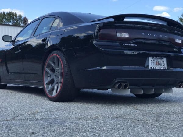 A black Dodge Charger R/T with red-trimmed rims parked in a lot, showcasing dual exhausts and a visible license plate PF J3476.