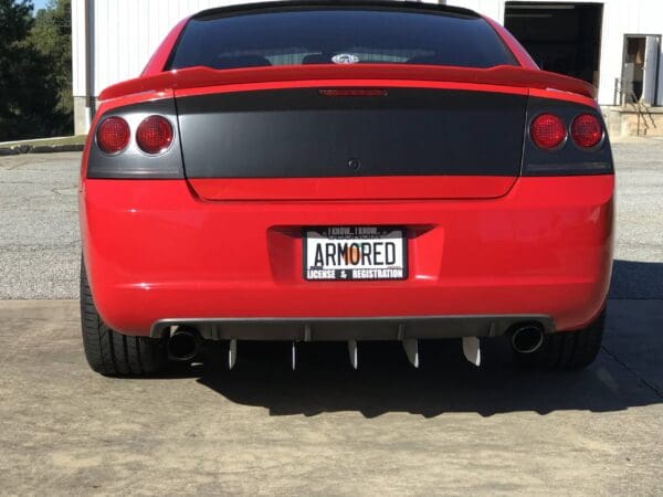 A red sports car with a license plate reading "ARMORED" is parked in front of a building.