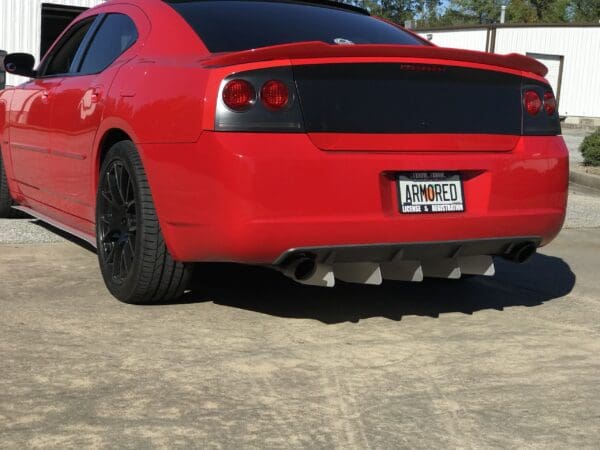 A red sports car with black wheels and a spoiler, featuring the license plate "ARMORED," parked on a concrete surface.