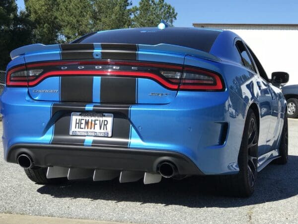 A blue Dodge Charger with black racing stripes is parked in a lot. The license plate reads "HEMIFVR."