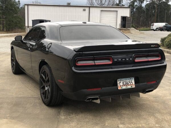 A black Dodge sports car with license plate CJG8655 parked in a lot near a white building.