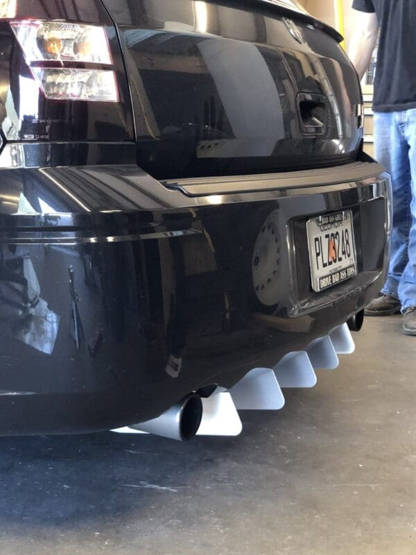Rear view of a black car with a Georgia license plate PLZ3248, showing custom exhaust fins and a person standing nearby.