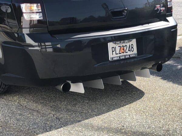 A black car with a Georgia license plate PLZ3248 is parked on the road. The plate frame reads "Bad Ass Girls Drive Bad Ass Toys."