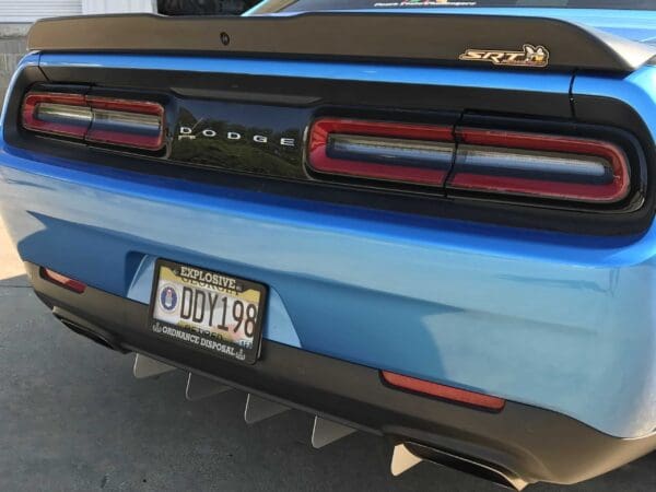 The rear end of a blue Dodge car with an SRT badge, parked in a driveway. The license plate reads "DDY198."
