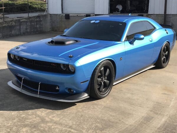 A blue Dodge Challenger with tinted windows is parked in front of a garage.