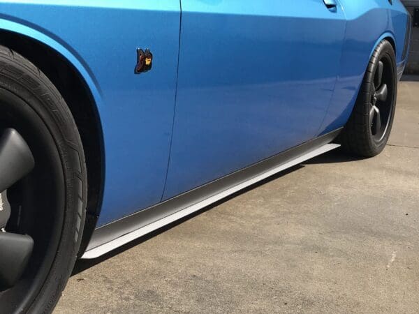 A blue sports car with a distinctive badge on the side is parked in a driveway.
