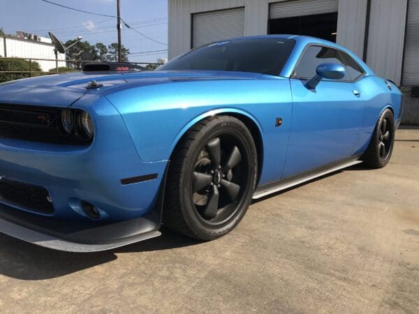 A blue car is parked in front of a garage with its sleek design highlighted.