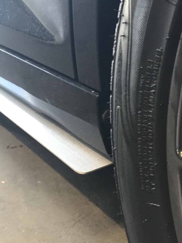 Close-up of a car tire next to the vehicle's body, showing the tread and side panel details.