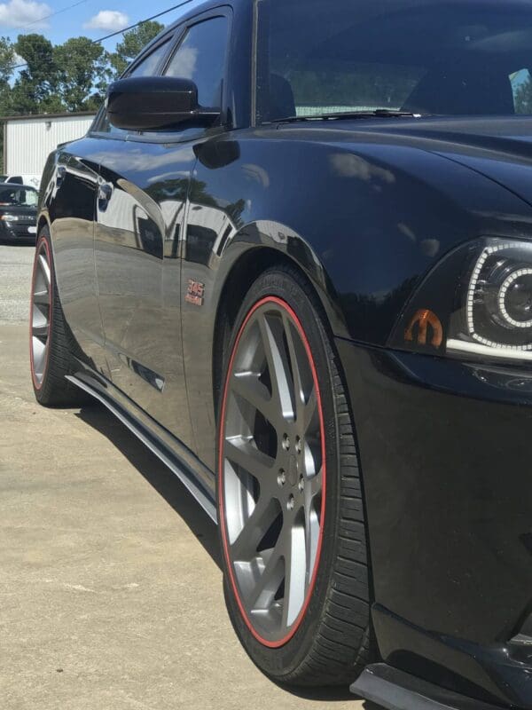 A sleek black sports car parked in a lot, featuring silver wheels with red accents and a "345 HEMI" badge on the side.