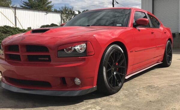 A red Dodge Charger SRT8 is parked in front of a white industrial building.