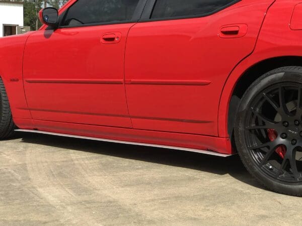 A red sports car parked in a lot, showcasing its side profile and black alloy wheels.