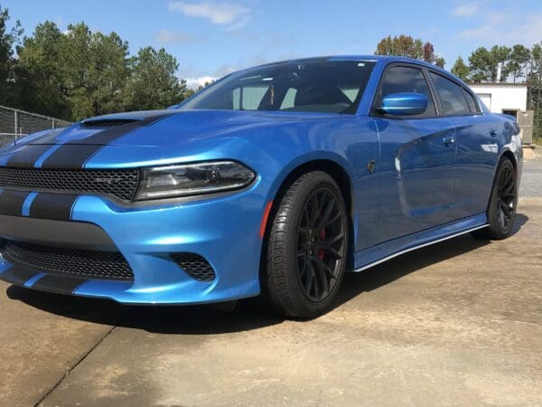 A blue Dodge Charger with black racing stripes parked in a driveway.